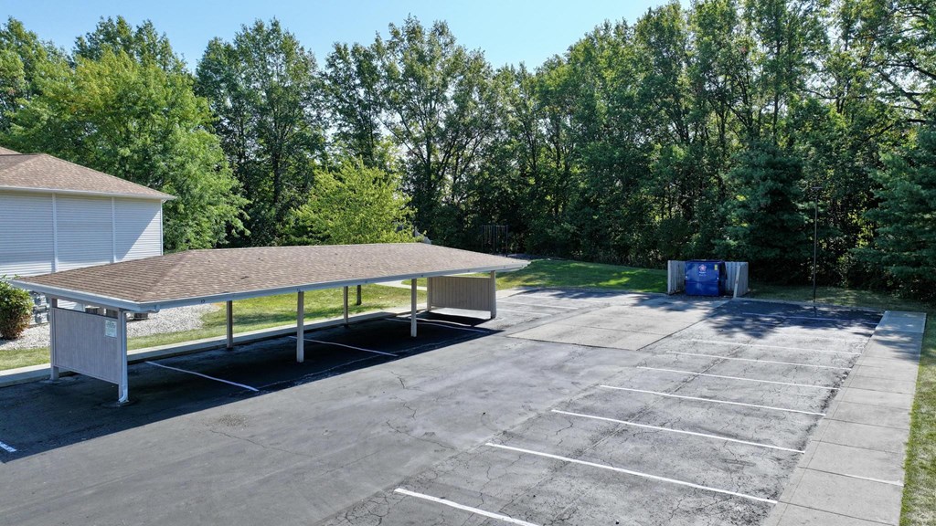 A parking lot with a white building and a blue dumpster in the background.