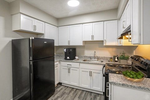 A black refrigerator stands in a kitchen with white cabinets and a marble countertop.