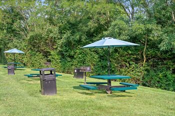A green picnic table with a blue umbrella is in the middle of a grassy area.