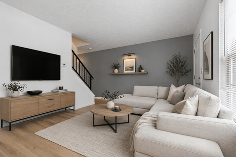 A living room with a white couch, a wooden cabinet, and a flat-screen TV mounted on the wall.