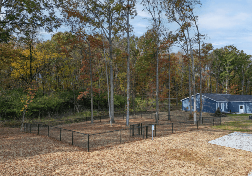 a fenced in dog park with a house and trees in the background