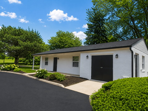 A white house with a black door and windows is surrounded by greenery.