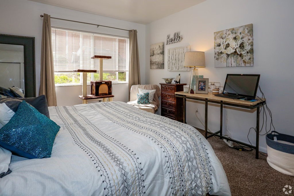 A bedroom with a bed, desk, and a window with blinds.