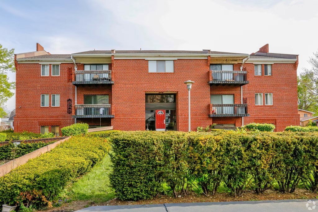 A red brick apartment building with a green hedge in front.