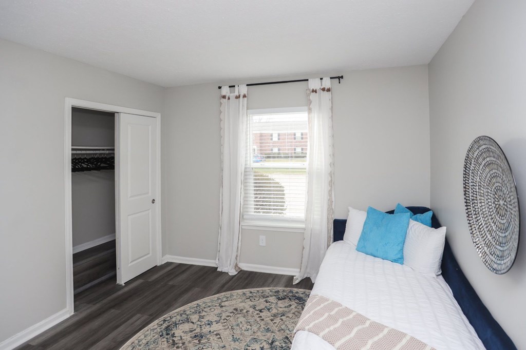 A bedroom with a bed, a window with curtains, and a fan on the wall.