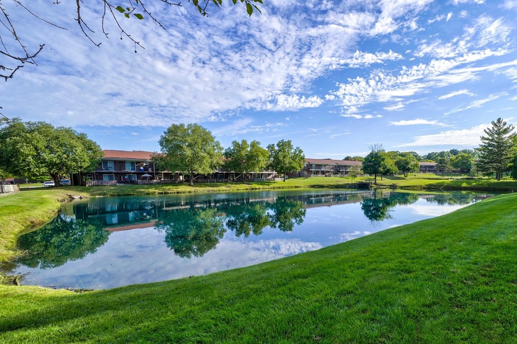 A serene landscape with a pond, trees, and buildings under a clear sky.at Meridian Court South, Indianapolis, IN