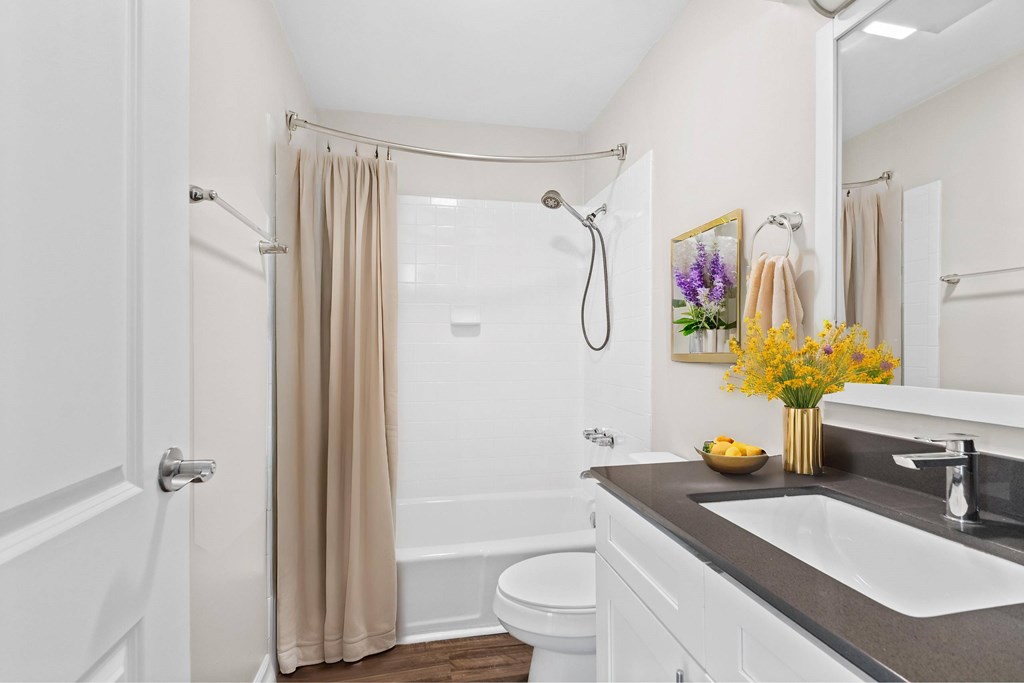 A white bathroom with a beige shower curtain and a white toilet at Fountain Parc Apartments, Indiana