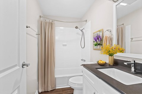 A white bathroom with a beige shower curtain and a white toilet at Fountain Parc Apartments, Indiana