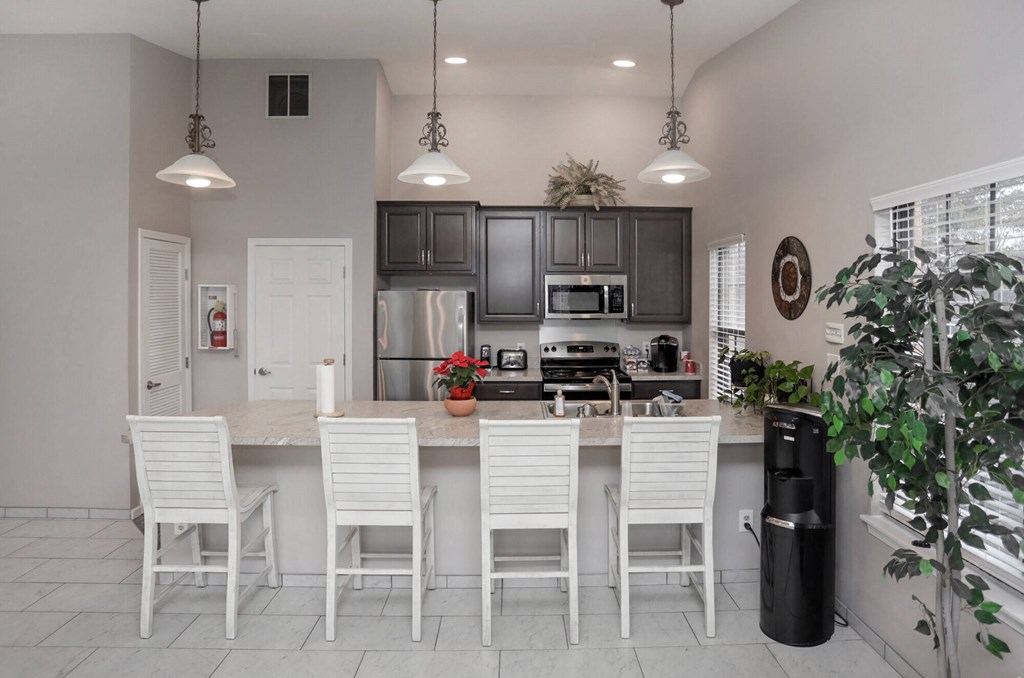 A kitchen with white chairs and a black trash can.