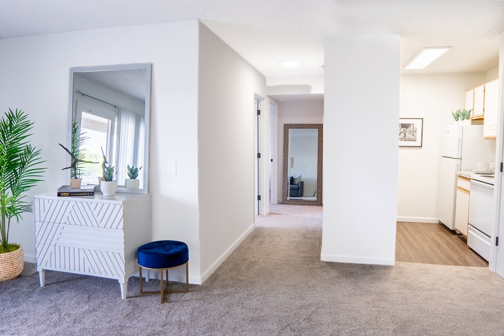 a hallway with white walls and a white dresser with a blue stool