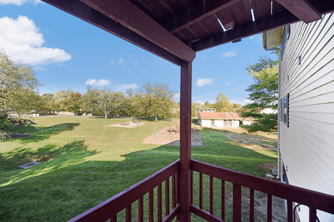 A view from a balcony overlooking a green lawn and a house.