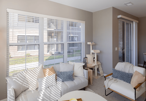 A living room with white furniture and a large window with blinds.