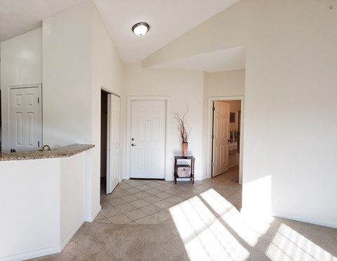 an empty living room with sunlight coming through the window and a door to a hallway