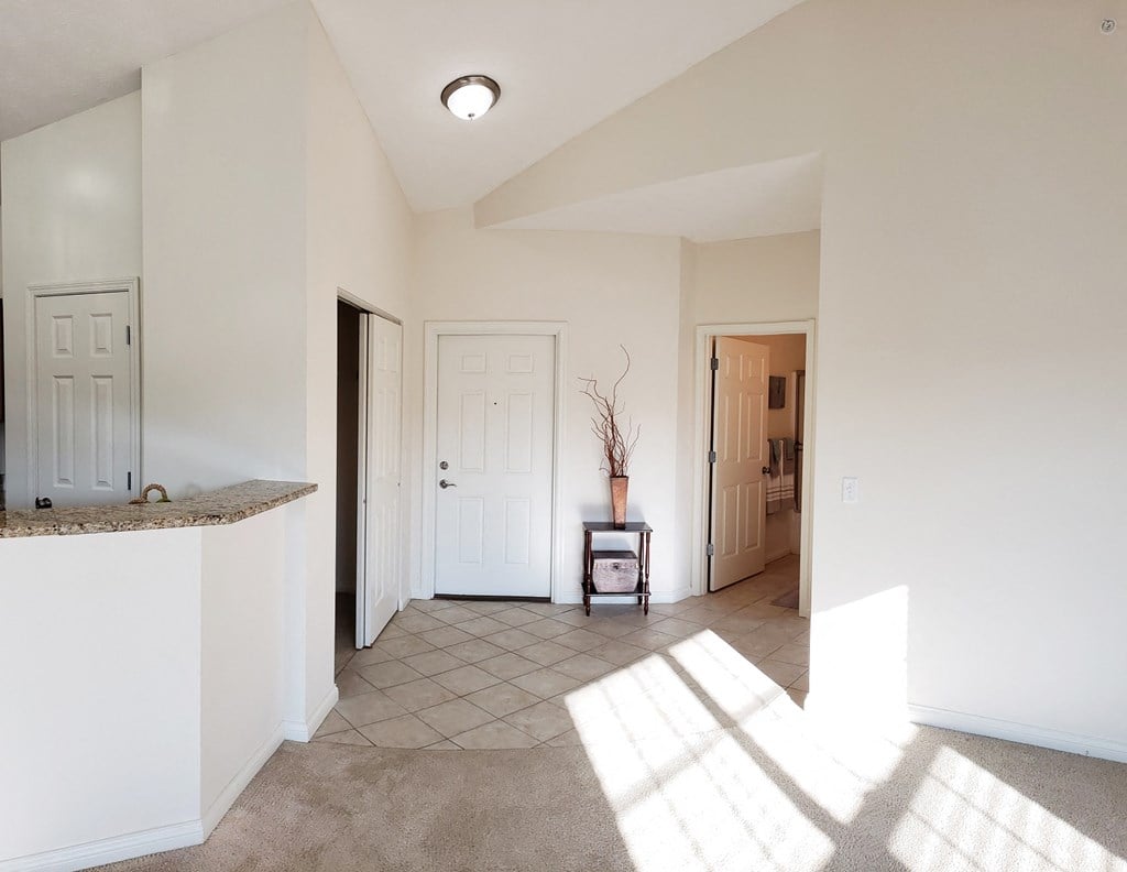 an empty living room with sunlight coming through the window and a door to a hallway