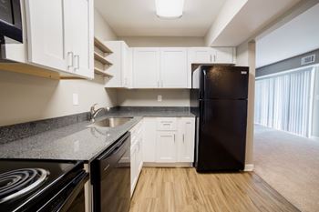 A black refrigerator sits in a kitchen with white cabinets.