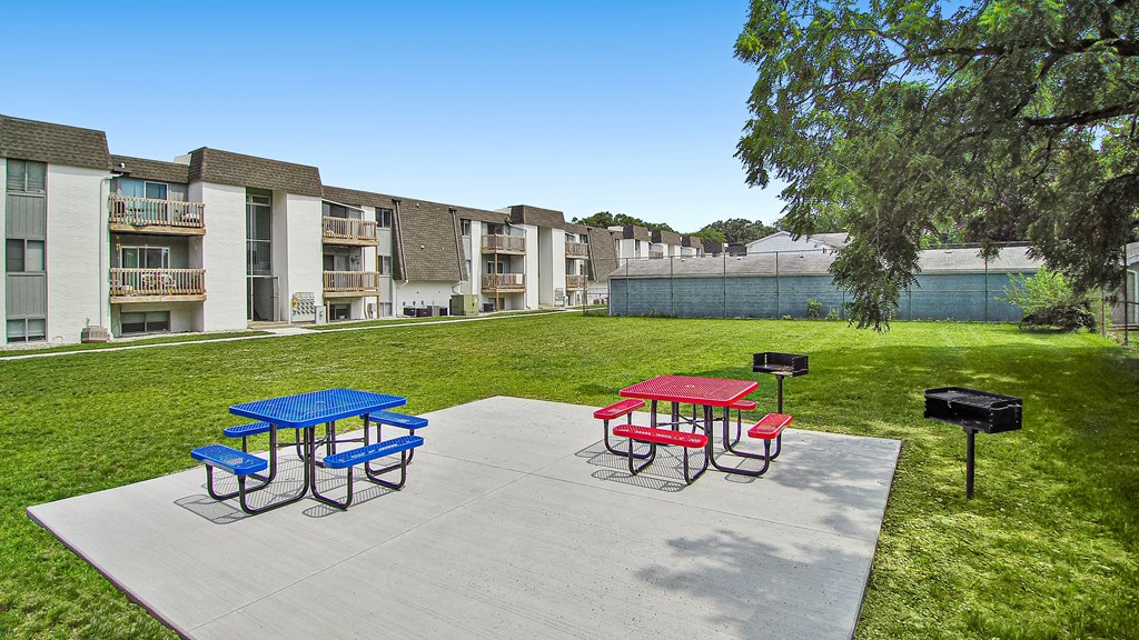 a picnic area with a blue picnic table and red picnic table on a concrete patio with a
