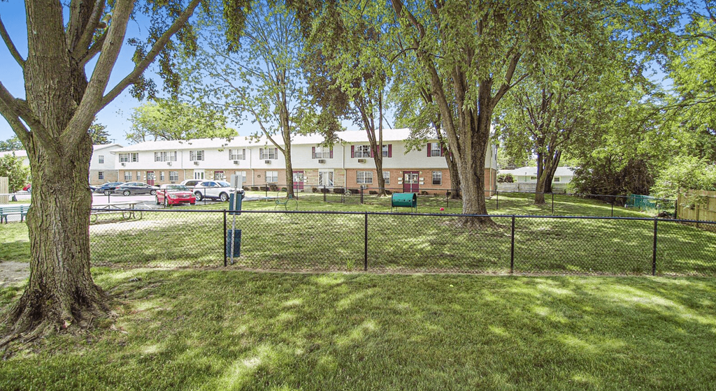 a fenced in dog park with trees and a building in the background