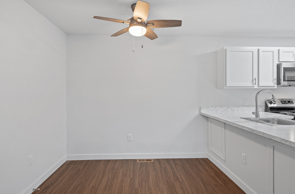 an empty living room with a ceiling fan and a kitchen