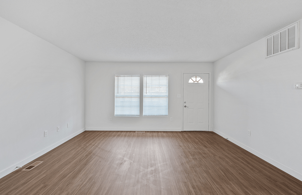 the spacious living room with hardwood flooring and a door to the bedroom
