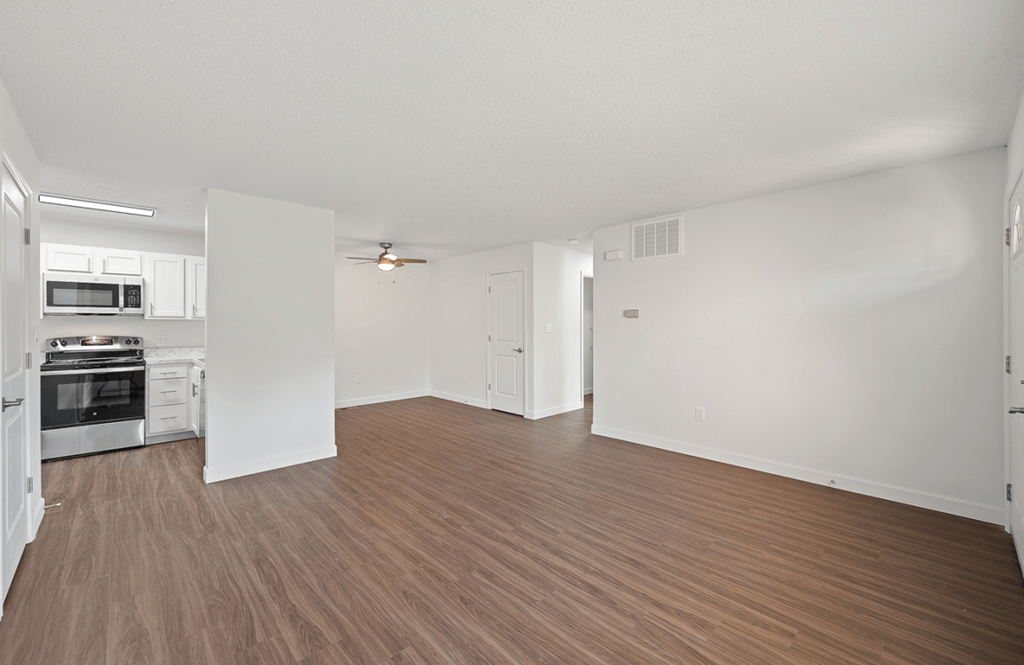 an empty living room and kitchen with wood flooring and white walls