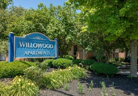 a sign for willowwood apartments in front of trees