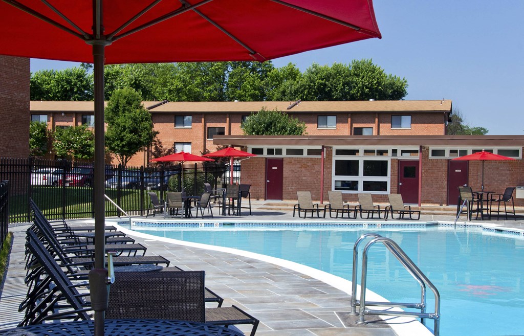 A pool area with chairs and umbrellas in front of a building at Rose Hill Apartments, Alexandria, 22310