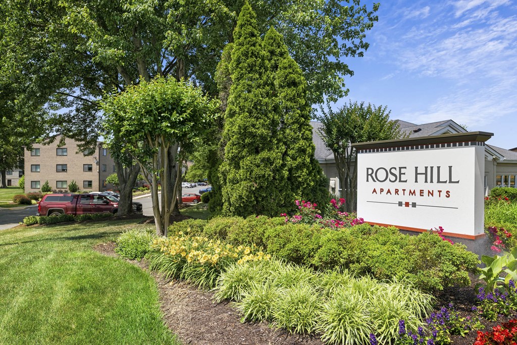 A sign for Rose Hill Apartments is surrounded by greenery and flowers at Rose Hill Apartments, Alexandria, Virginia