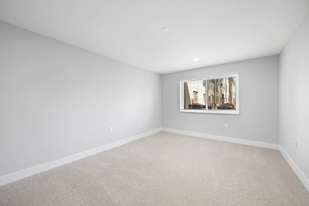 A room with a carpeted floor and a window showing a building outside at Rose Hill Apartments, Alexandria, VA