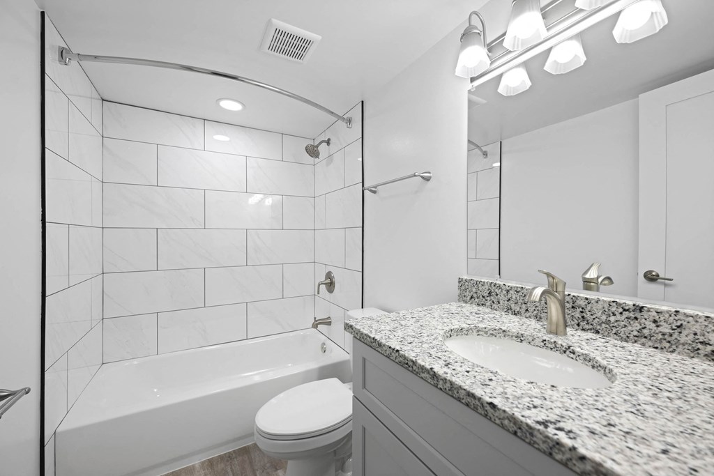A white bathroom with a marble counter top and a white toilet at Rose Hill Apartments, Alexandria, VA