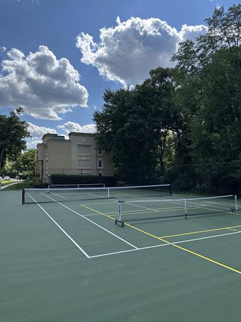 a tennis court with trees and a building in the background at Stuart Woods* Apartments, Virginia, 20170