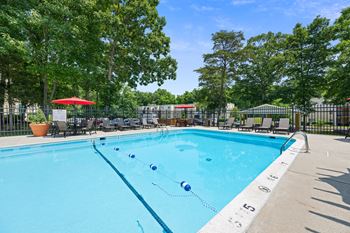 a swimming pool with chairs and umbrellas and trees at Stuart Woods* Apartments, Herndon, Virginia