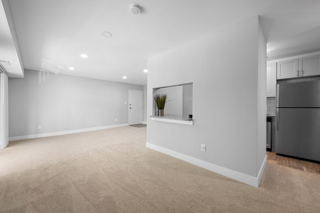 a living room with white walls and carpet and a black refrigerator at Gainsborough Court Apartments, Fairfax, VA, 22030