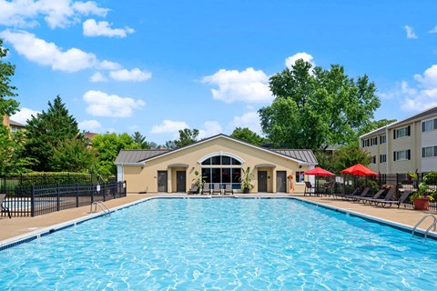 A large swimming pool in front of a building with a black fence and trees in the background.