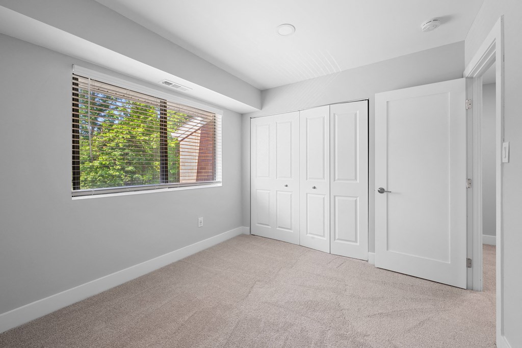 an empty bedroom with a large window and white doors at Gainsborough Court Apartments, Virginia