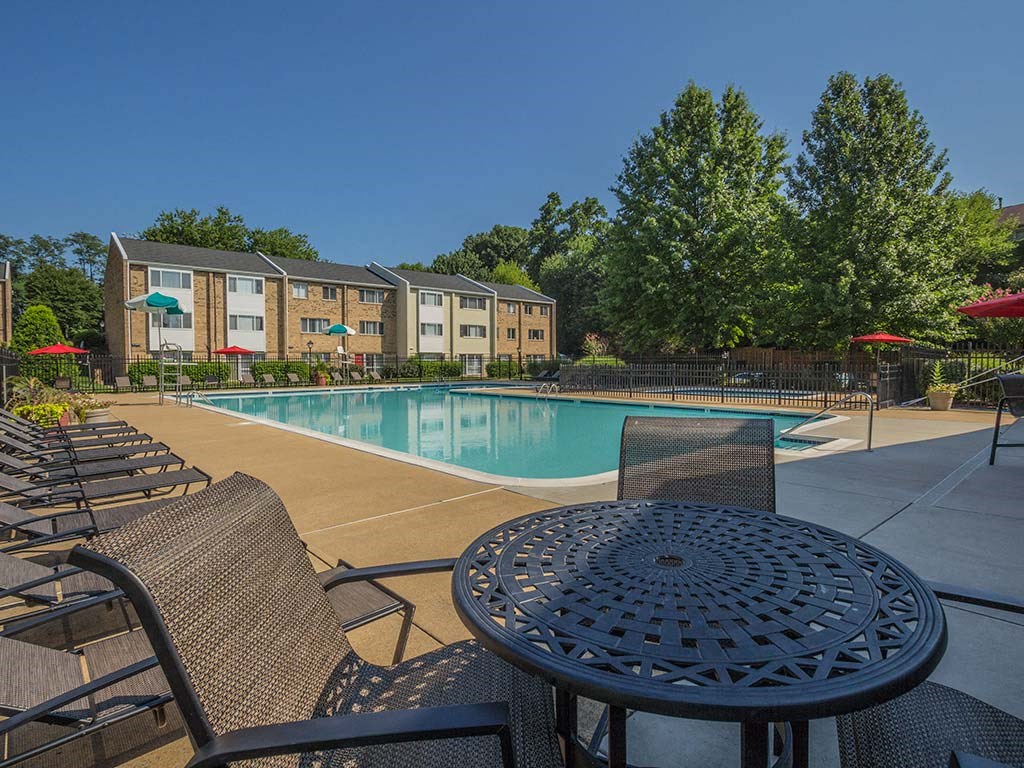 Outdoor table seating area with lounge chairs by the pool at Tysons Glen Apartments and Townhomes, Falls Church
