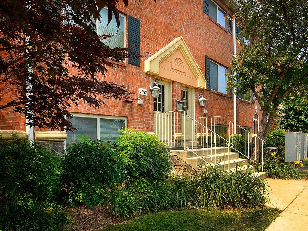 A red brick building with a green bush in front at Gainsborough Court Apartments, Virginia, 22030