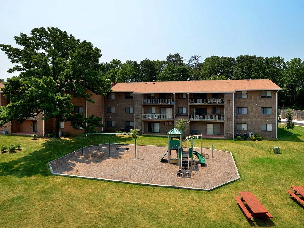 A playground with a green slide and a red bench in front of a building at Gainsborough Court Apartments, Fairfax, Virginia