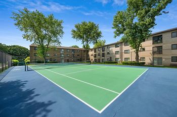 a tennis court with trees and apartments in the background at Rose Hill Apartments, Virginia