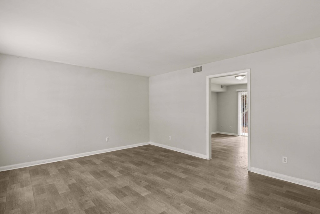 the living room of an apartment with white walls and wood flooring
