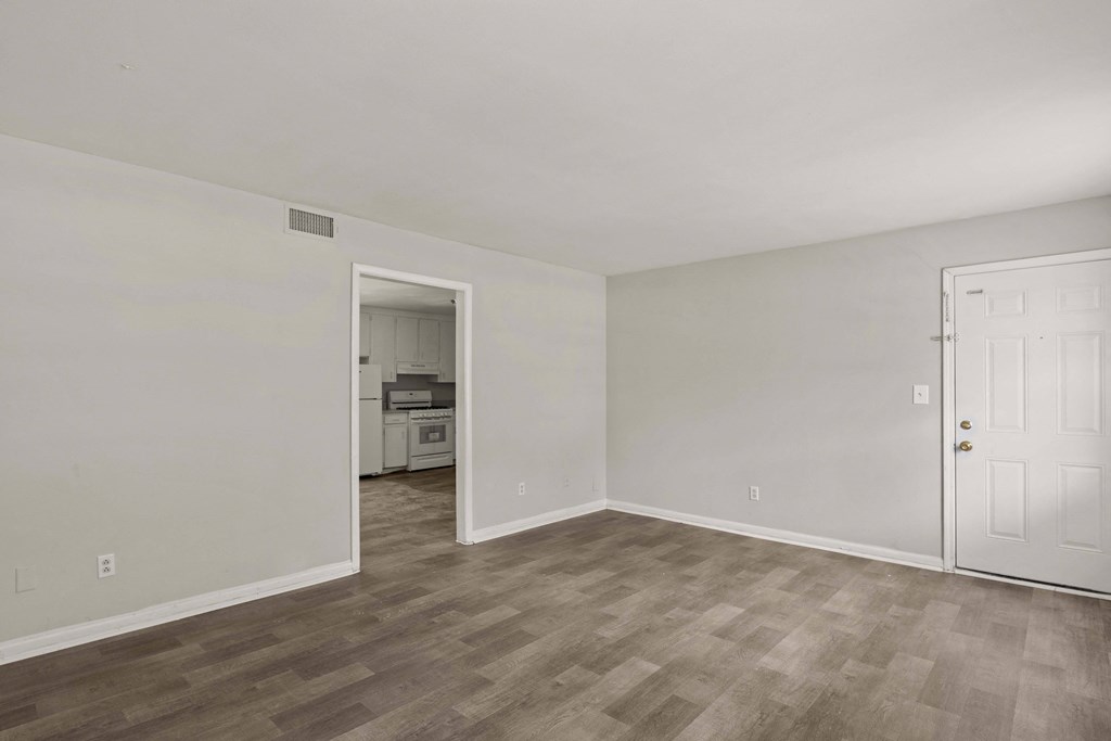 the living room of an apartment with white walls and wood flooring