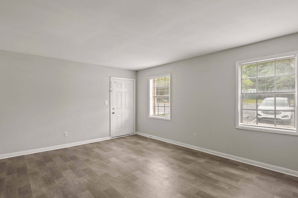 the spacious living room of an apartment with a white door and window