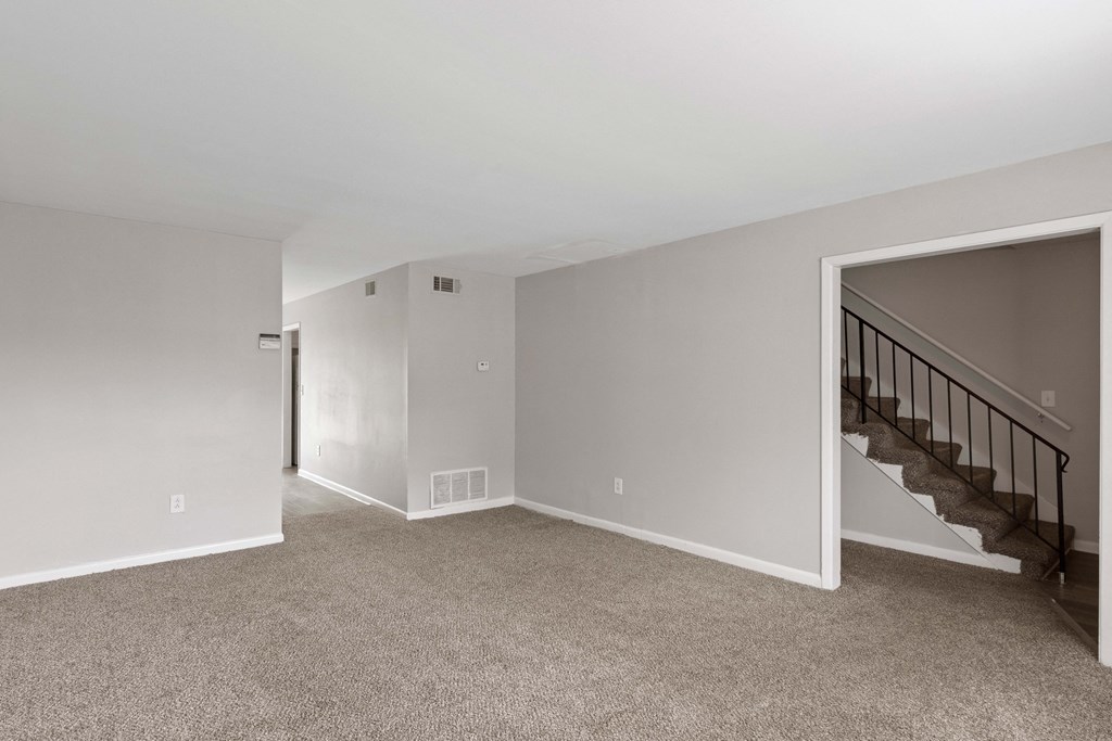 an empty living room with carpet and stairs in a house