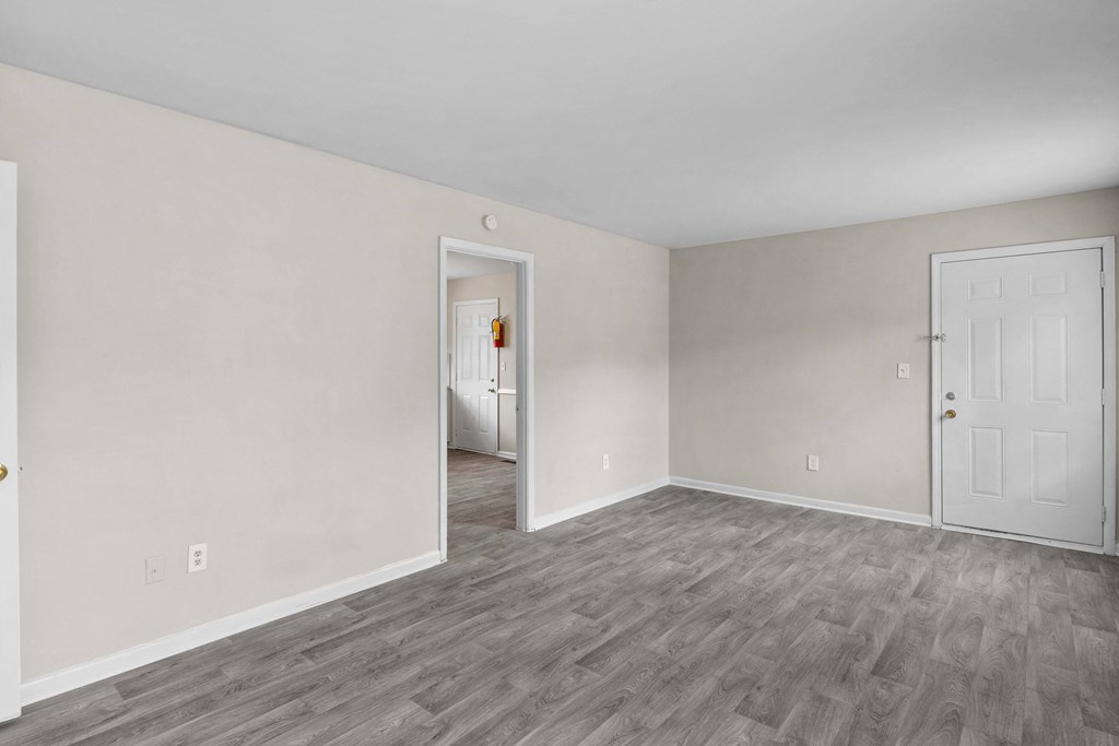 the living room of an apartment with white walls and wood flooring