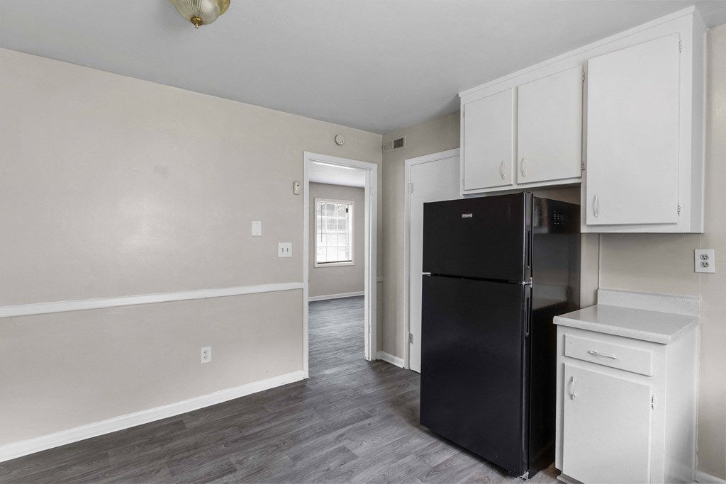 an empty kitchen with black refrigerator and white cabinets