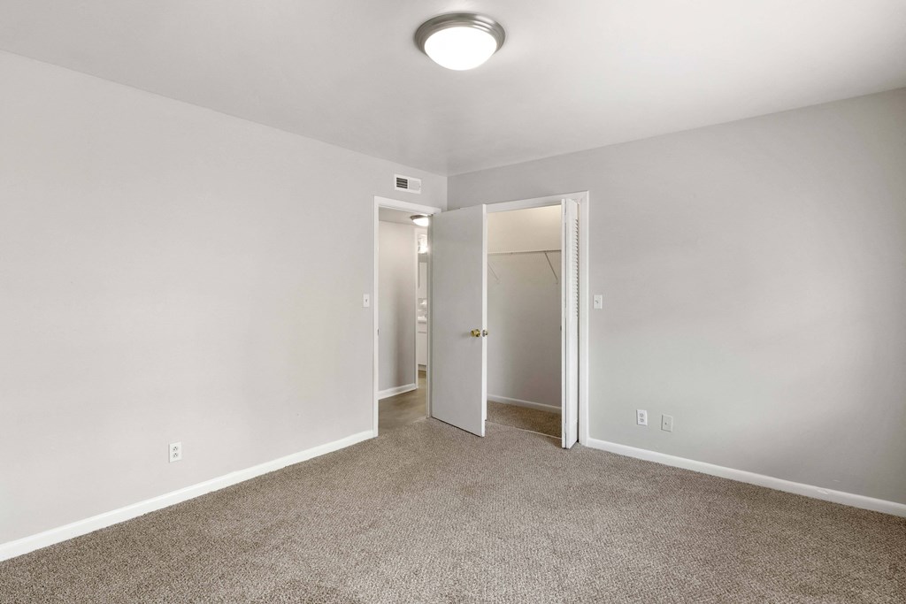 a bedroom with white walls and carpet and a door to a closet