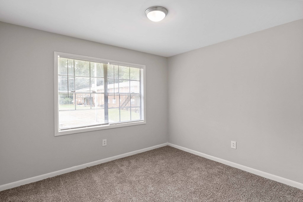 an empty bedroom with a window and carpeting