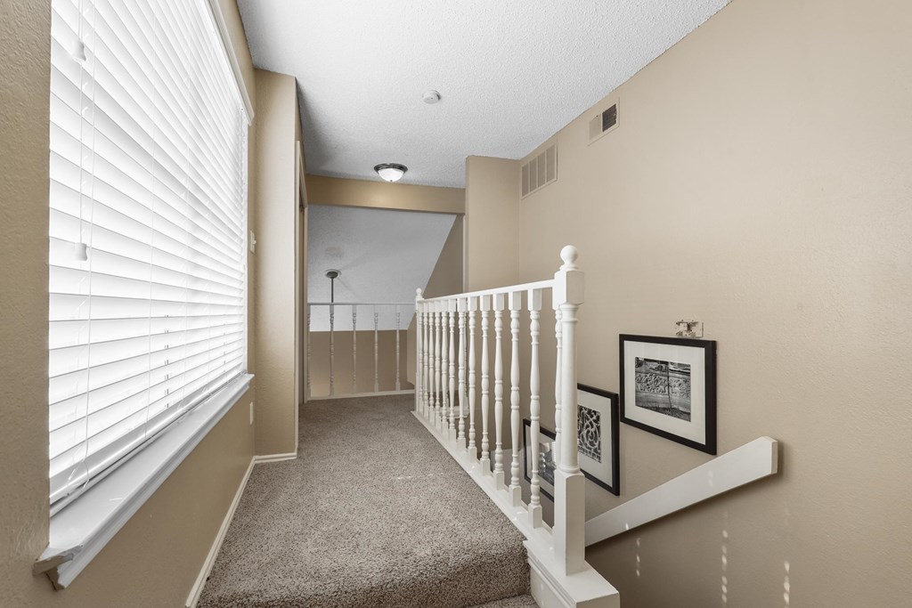 A hallway with a staircase and pictures on the wall.