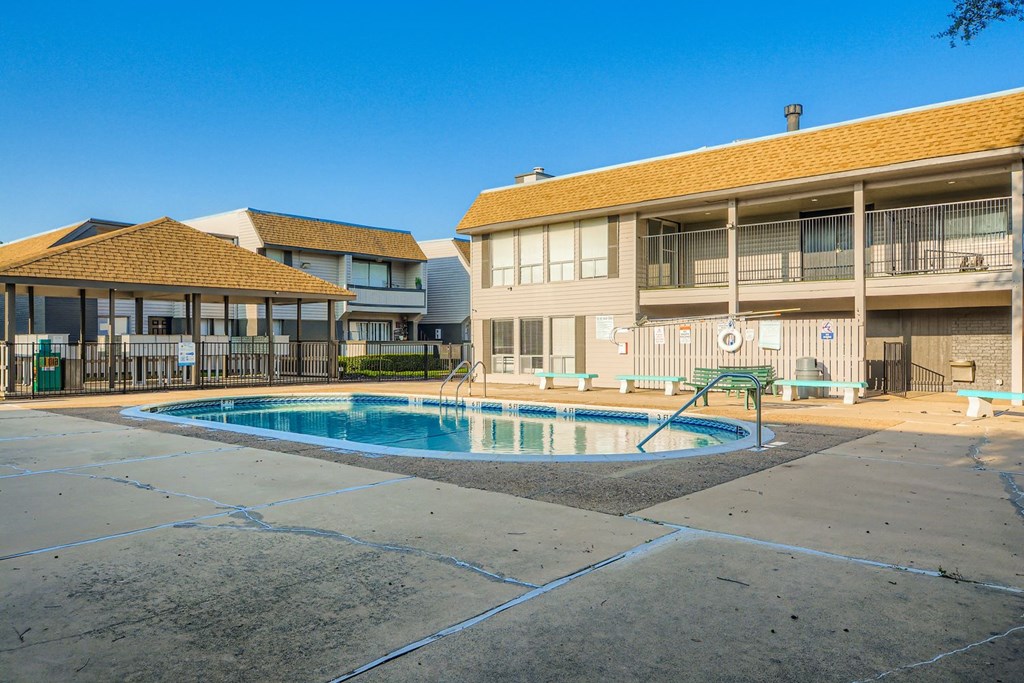 A swimming pool is surrounded by a concrete patio and a building.