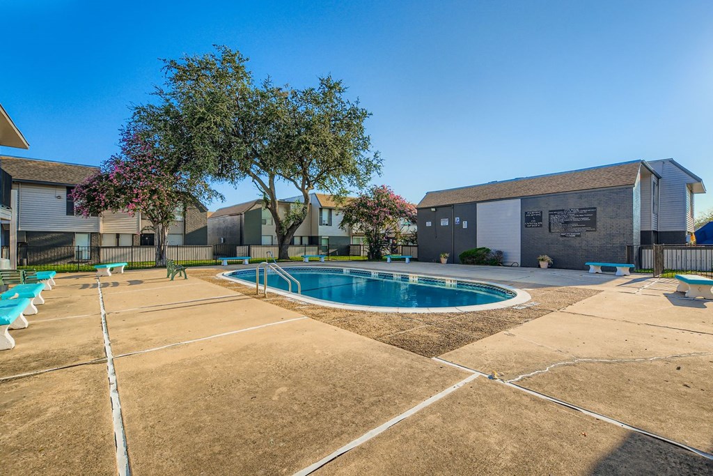 A pool surrounded by a concrete ground and a building in the background.