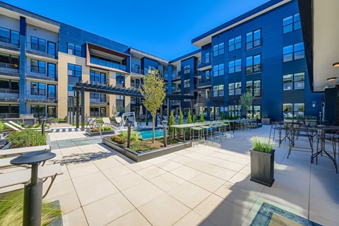 A sunny day at a modern apartment complex with a pool and outdoor seating area.
